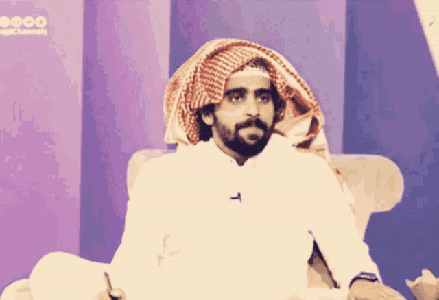 a man with a beard and a scarf around his head is sitting in a chair