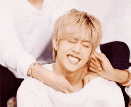 a person is putting their hands on a young man 's neck while he smiles .