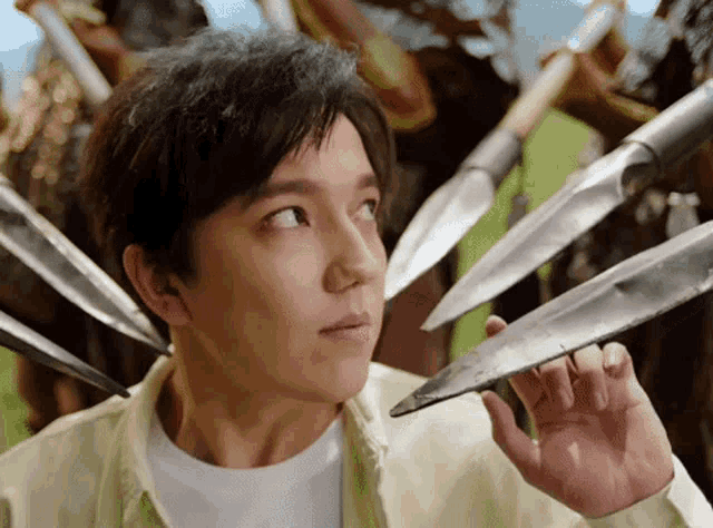 a young man is holding a knife in front of a group of spears