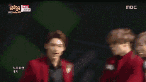 a group of young men in red suits are standing on a stage with a mbc logo in the background