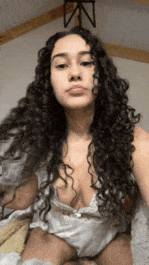 a woman with curly hair is taking a selfie in a bedroom