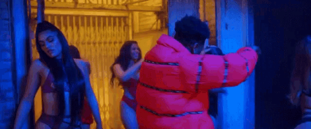 a man in a red jacket is standing next to two women in bikinis in a dark room .
