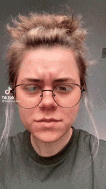 a woman wearing glasses and a green shirt has a tik tok sticker on her face
