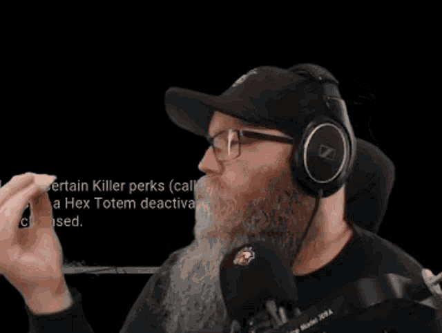 a man with a beard wearing headphones and glasses is talking into a microphone .