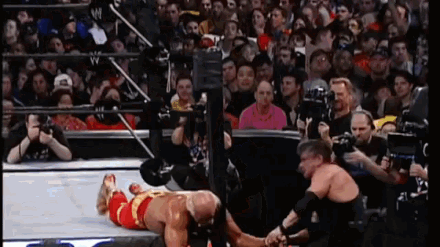 a wrestler is laying on the ground while another wrestler holds his hand out to him
