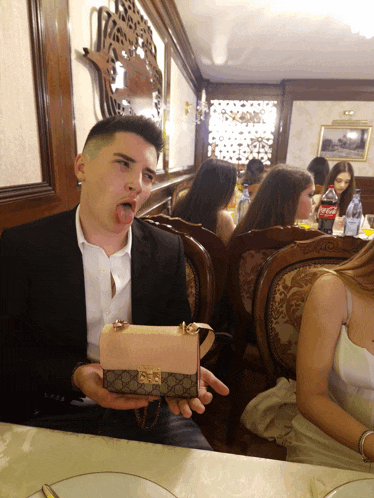a man sitting at a table holding a pink purse with a gucci logo on it