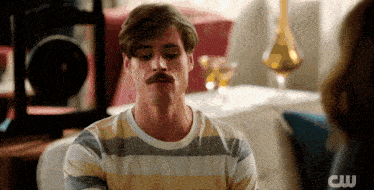 a man with a mustache is wearing a striped shirt with the cw logo on the bottom