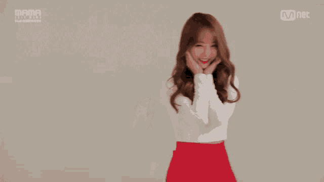 a woman in a white shirt and red skirt is clapping in front of a screen that says mnet