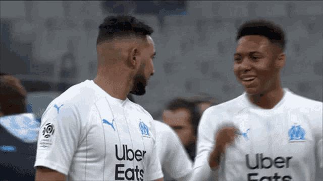 two soccer players wearing uber eats jerseys are standing next to each other .