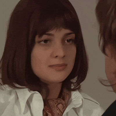 a woman in a white shirt and scarf looks at another woman