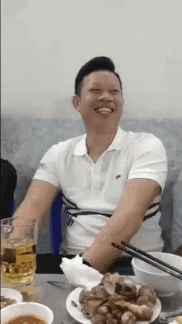 a man is sitting at a table with a glass of beer and plates of food .