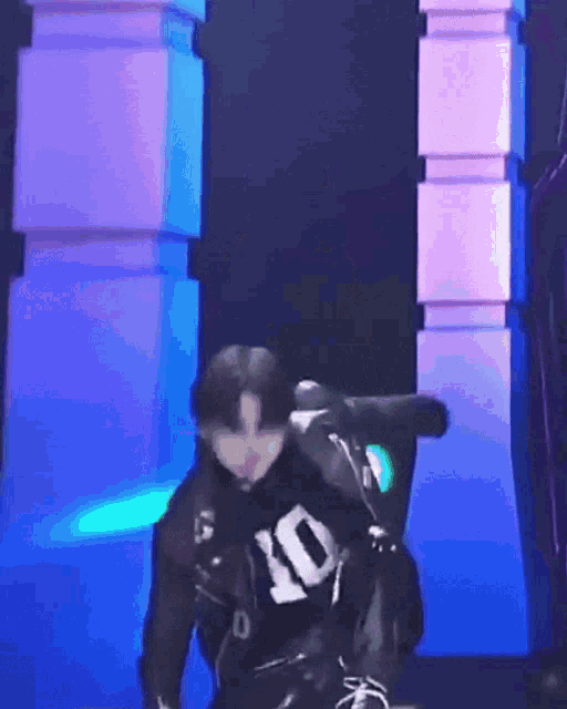 a man wearing a black shirt with the number 10 on it is dancing on a stage