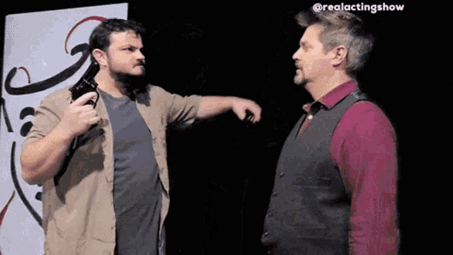 a man pointing a gun at another man in front of a sign that says @realactingshow