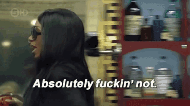 a woman says absolutely fuckin ' not while standing in front of a shelf full of bottles