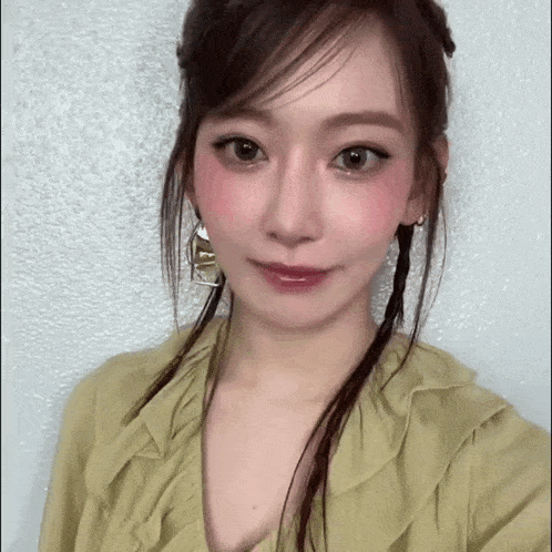 a close up of a woman 's face wearing a green top and earrings