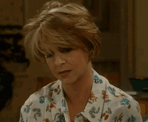 a woman wearing a floral shirt and earrings looks at the camera .