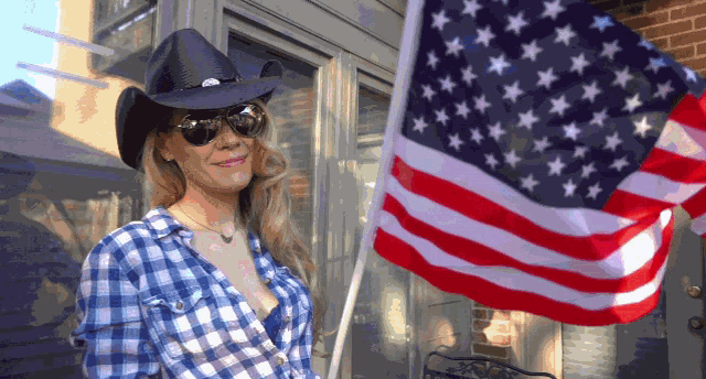 a woman wearing a cowboy hat and plaid shirt holds an american flag