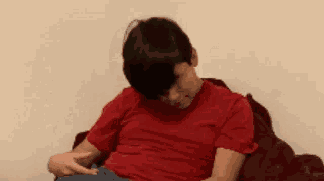a man in a red shirt is sitting on a couch with his head on his hand .