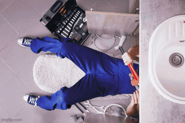 a plumber laying on the floor holding a wrench and a toolbox