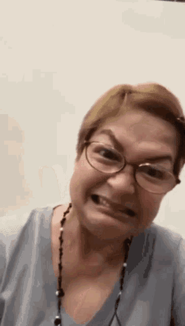 a woman wearing glasses and a necklace is making an angry face .