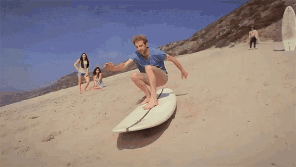 a man is riding a surfboard on the beach while two women look on