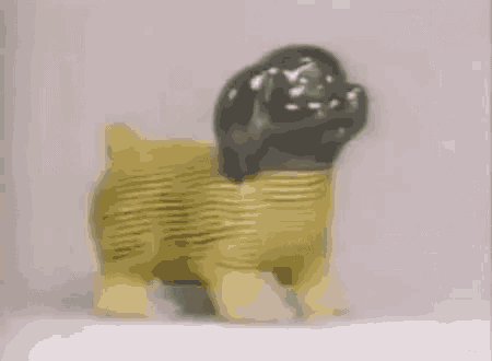 a toy sheep with yellow legs and a black head is standing on a white surface .