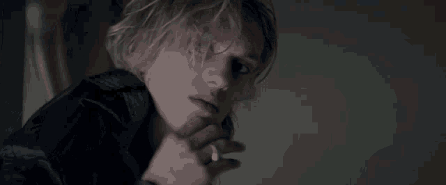 a young man with blonde hair is smoking a cigarette .