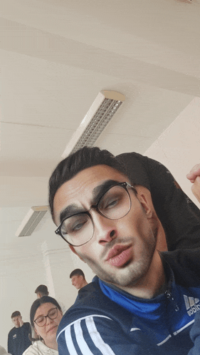 a man wearing glasses and a blue adidas jacket is making a funny face
