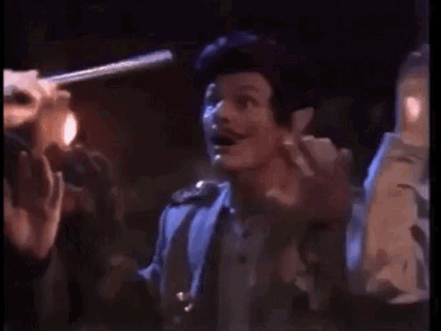a man with a mustache is standing in front of a group of people holding a lighter .