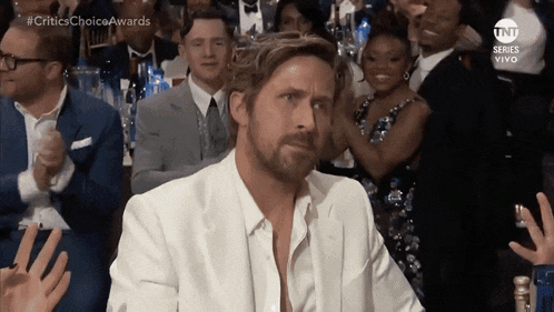 a man in a white suit sits in a crowd at a critics choice awards