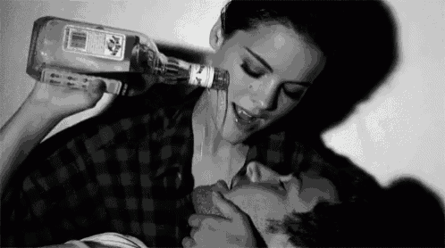 a black and white photo of a woman drinking from a bottle while kissing a man .