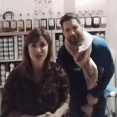 a man and a woman are posing for a picture in front of a shelf full of jars