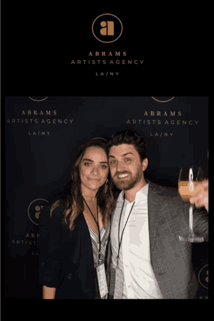 a man and a woman are posing for a photo in front of a wall that says abrams artists agency