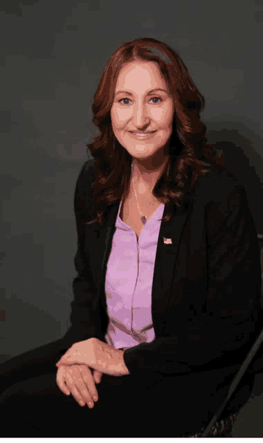 a woman wearing a black jacket and a purple shirt with an american flag pin