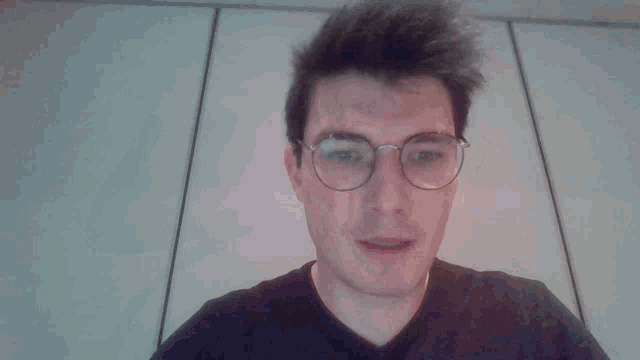 a man wearing glasses waves his hand in front of his face