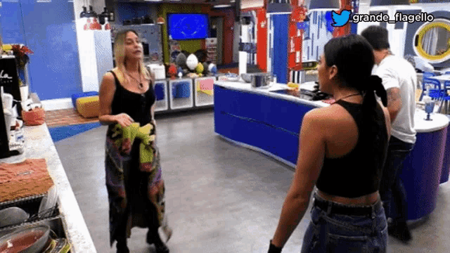 a woman in a black tank top is standing next to another woman in a kitchen with a twitter logo above them