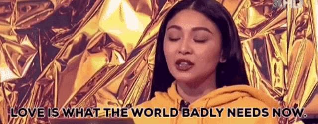 a woman in a yellow hoodie is standing in front of a gold foil background .