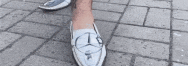 a person wearing a pair of white shoes with a mercedes logo on them