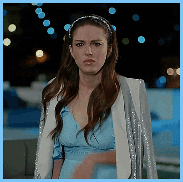 a woman wearing a blue dress and a white jacket looks angry