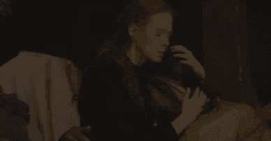 a woman is sitting on a couch with a man in a dark room holding her breast .