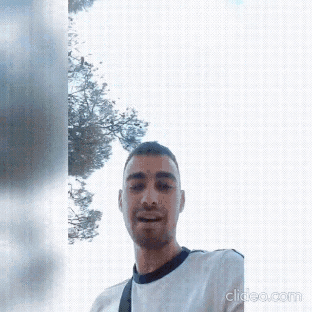 a man in a white shirt is standing in front of a tree
