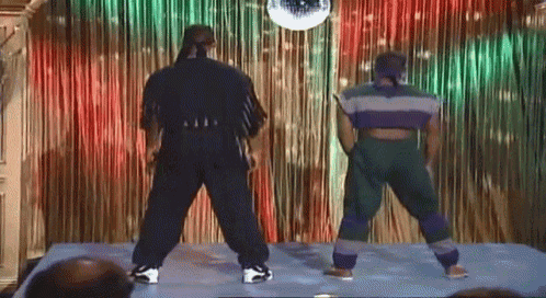 two men are dancing on a stage with a disco ball in the background
