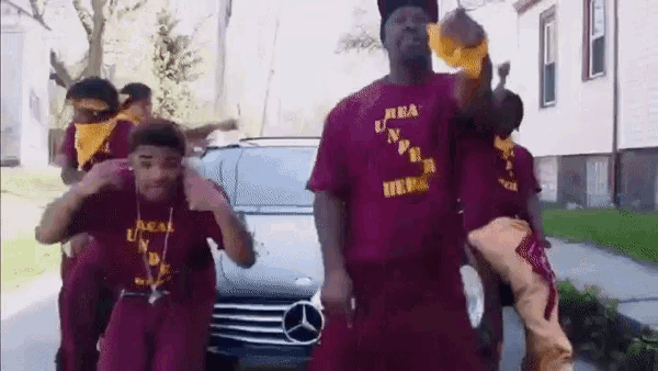 a group of young men are dancing in front of a mercedes car .