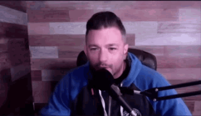 a man in a blue hoodie is talking into a microphone .