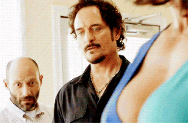 a man with a mustache is standing next to a woman in a blue top