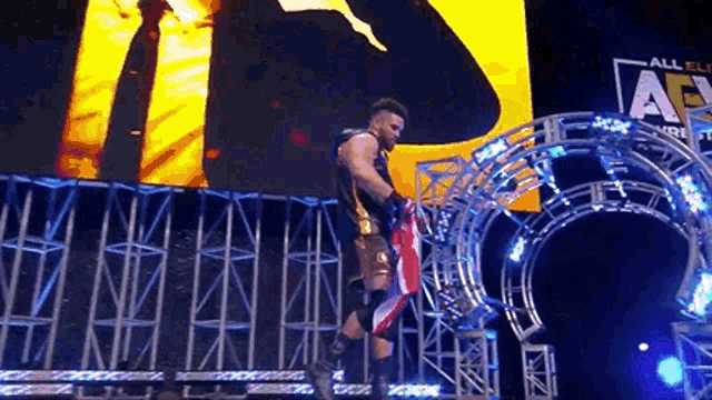 a wrestler is holding an american flag on a stage in front of a large screen .
