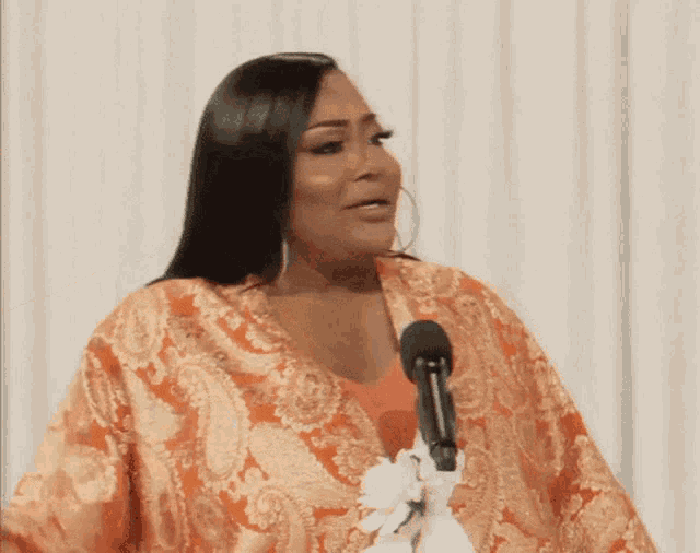 a woman wearing a paisley jacket is speaking into a microphone
