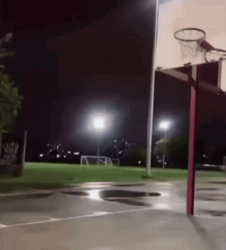 a basketball court is lit up at night with a basketball hoop in the foreground
