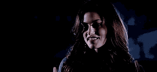 a woman with long hair is standing in the dark and looking at the camera with a serious look on her face .