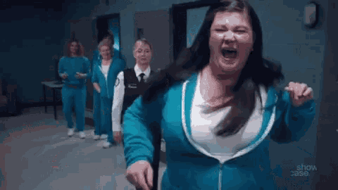 a woman in a blue jacket is making a surprised face while walking in a room with other women .